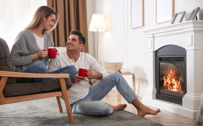 Happy couple with cups of hot drink resting near fireplace at home